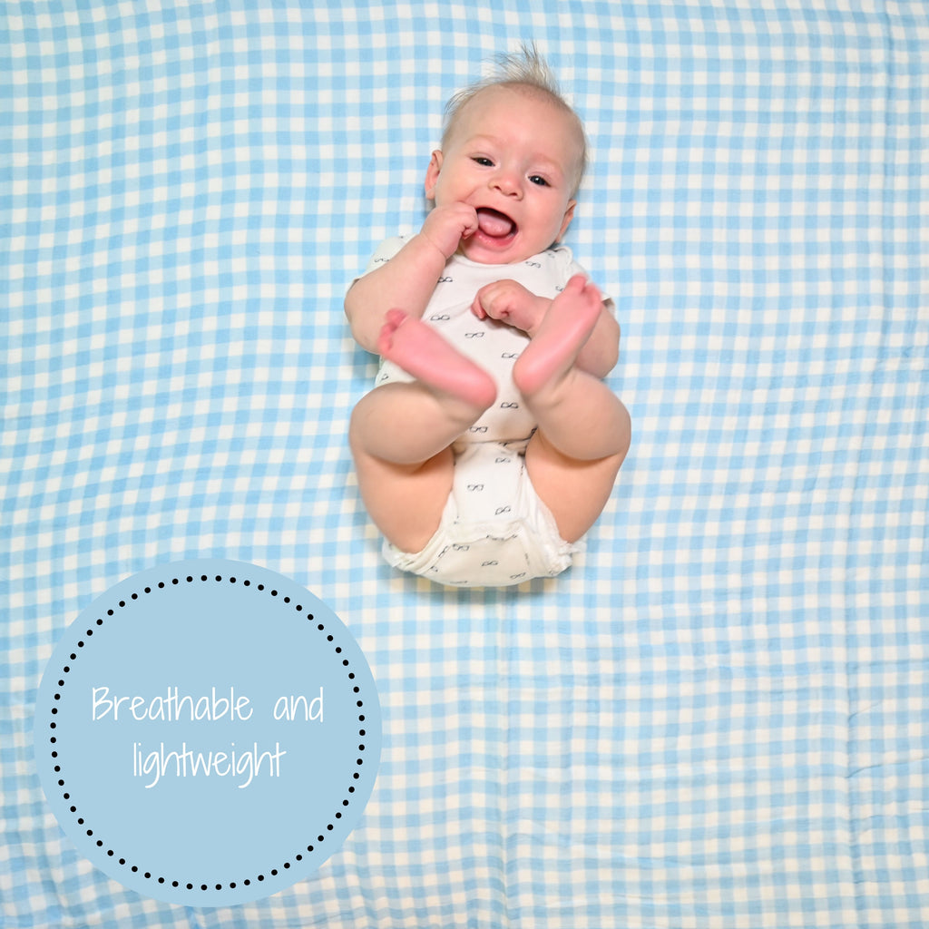A cheerful baby boy with an infectious smile, set against the backdrop of the Classic Comfort Blue Gingham 100% Muslin Cotton Swaddle Blanket - 47" x 47", radiating happiness and timeless style.