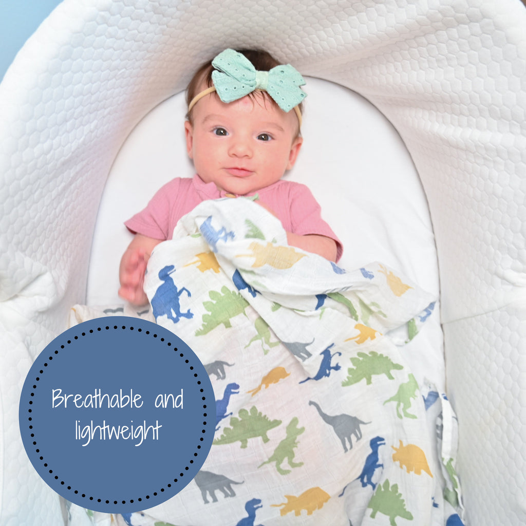 A happy baby girl with an enchanting smile, snugly cocooned in the Dino Adventure Muslin Swaddle Blanket - 47" x 47", resting peacefully in her bassinet, radiating joy and comfort.