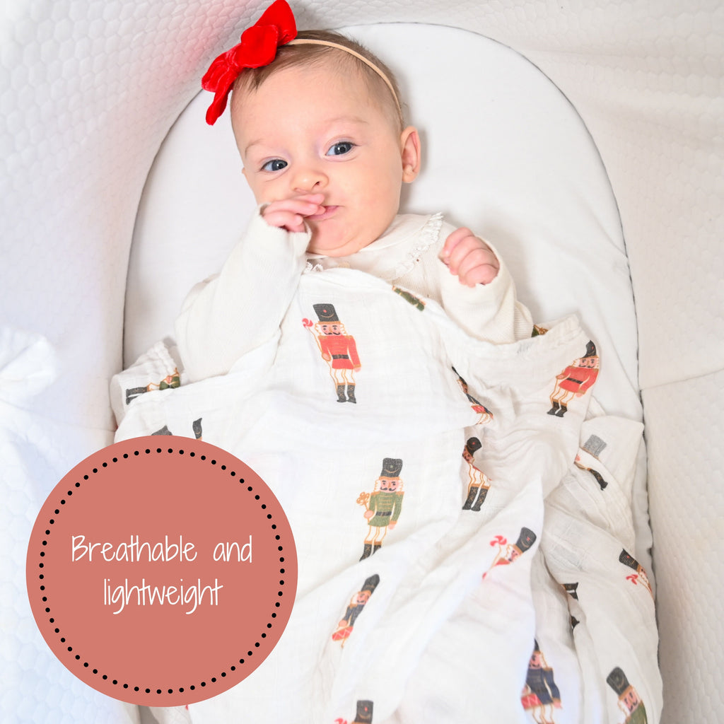 A baby girl wrapped in the cozy embrace of the Nutcracker Magic 100% Muslin Cotton Swaddle Blanket - 47" x 47", experiencing warmth and comfort with an enchanting touch.