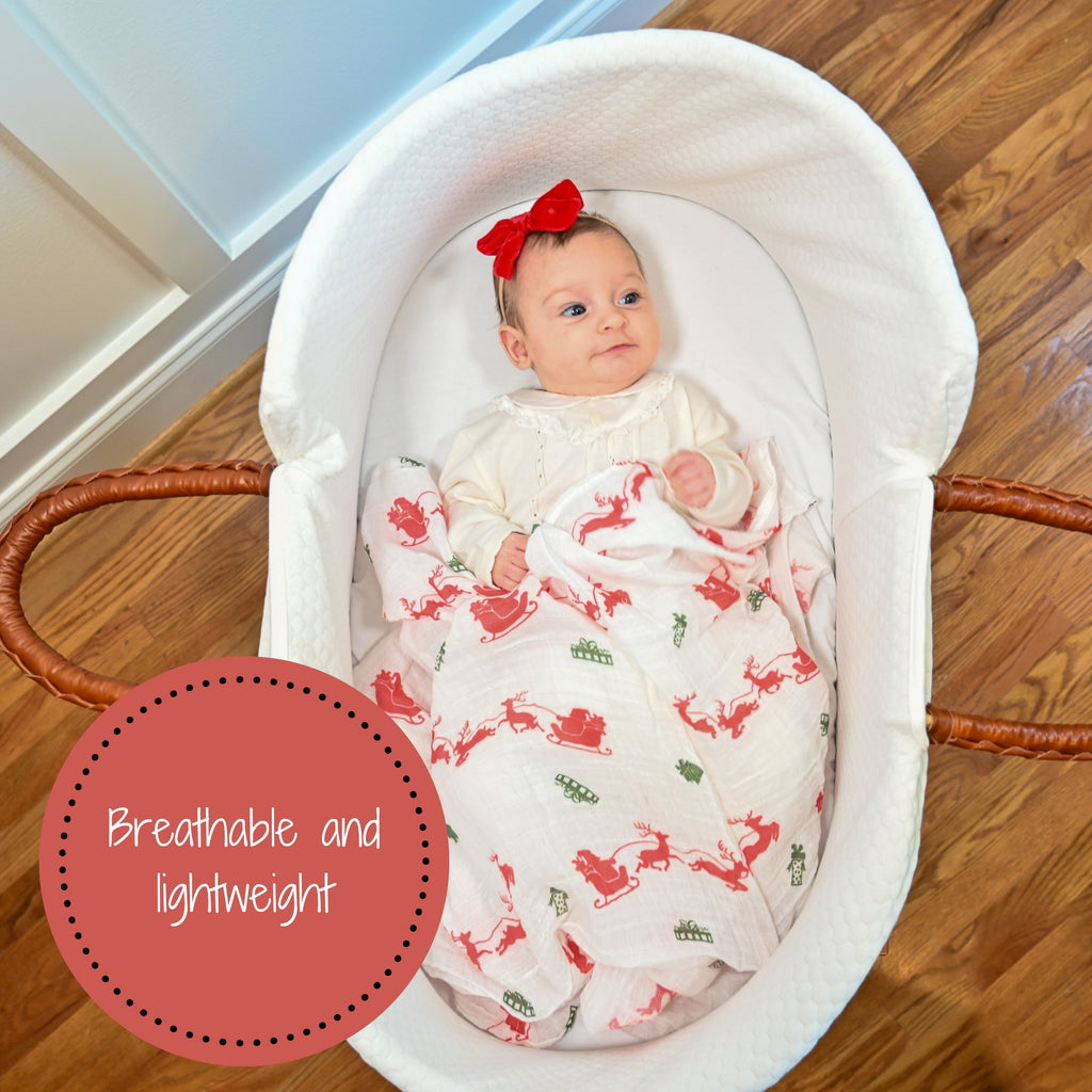A joyful baby girl with a radiant smile, nestled in the Santa and Reindeer Muslin Swaddle Blanket - 47" x 47", adding a touch of holiday delight to her crib