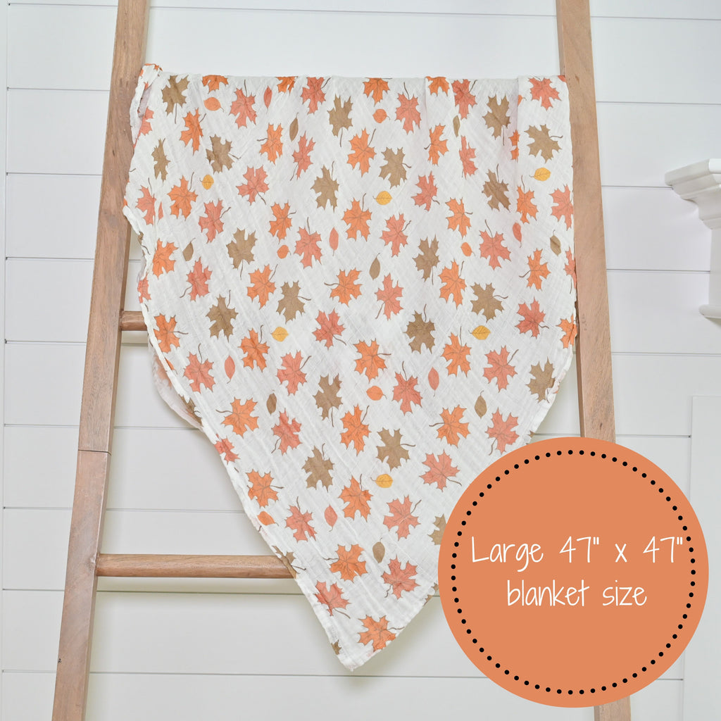 The Fall Leaves Muslin Swaddle Blanket - 47" x 47" elegantly displayed on a decorative ladder, bringing a touch of autumn style to any nursery or room.