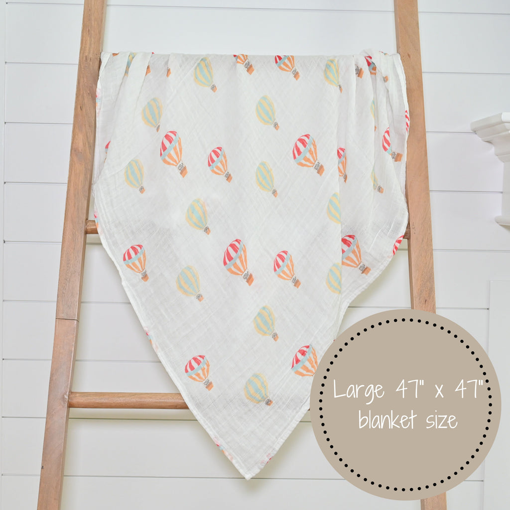 The Up, Up, and Away 100% Muslin Cotton Swaddle Blanket - 47" x 47" beautifully displayed on a decorative ladder, adding a touch of whimsy to any nursery or room.
