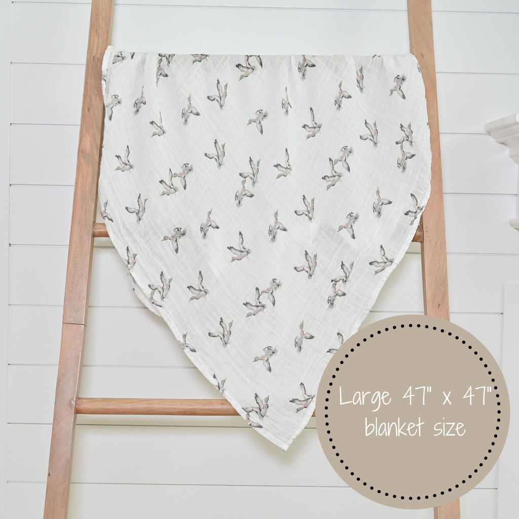 The Mallard Magic 100% Muslin Cotton Swaddle Blanket - 47" x 47" beautifully displayed on a decorative ladder, adding a touch of waterfowl whimsy to any nursery or room.