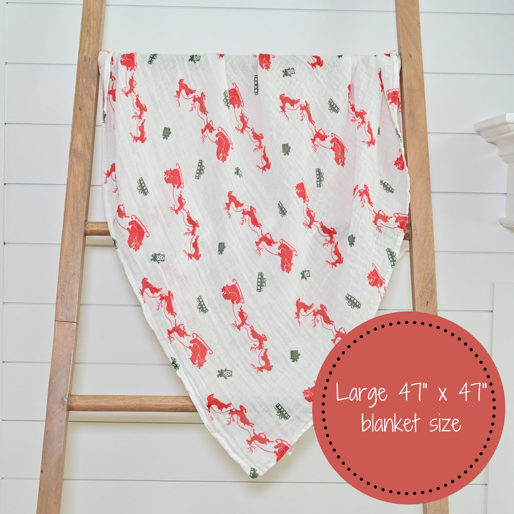The Santa and Reindeer Muslin Swaddle Blanket - 47" x 47" beautifully displayed on a decorative ladder, adding holiday charm to any nursery or room.