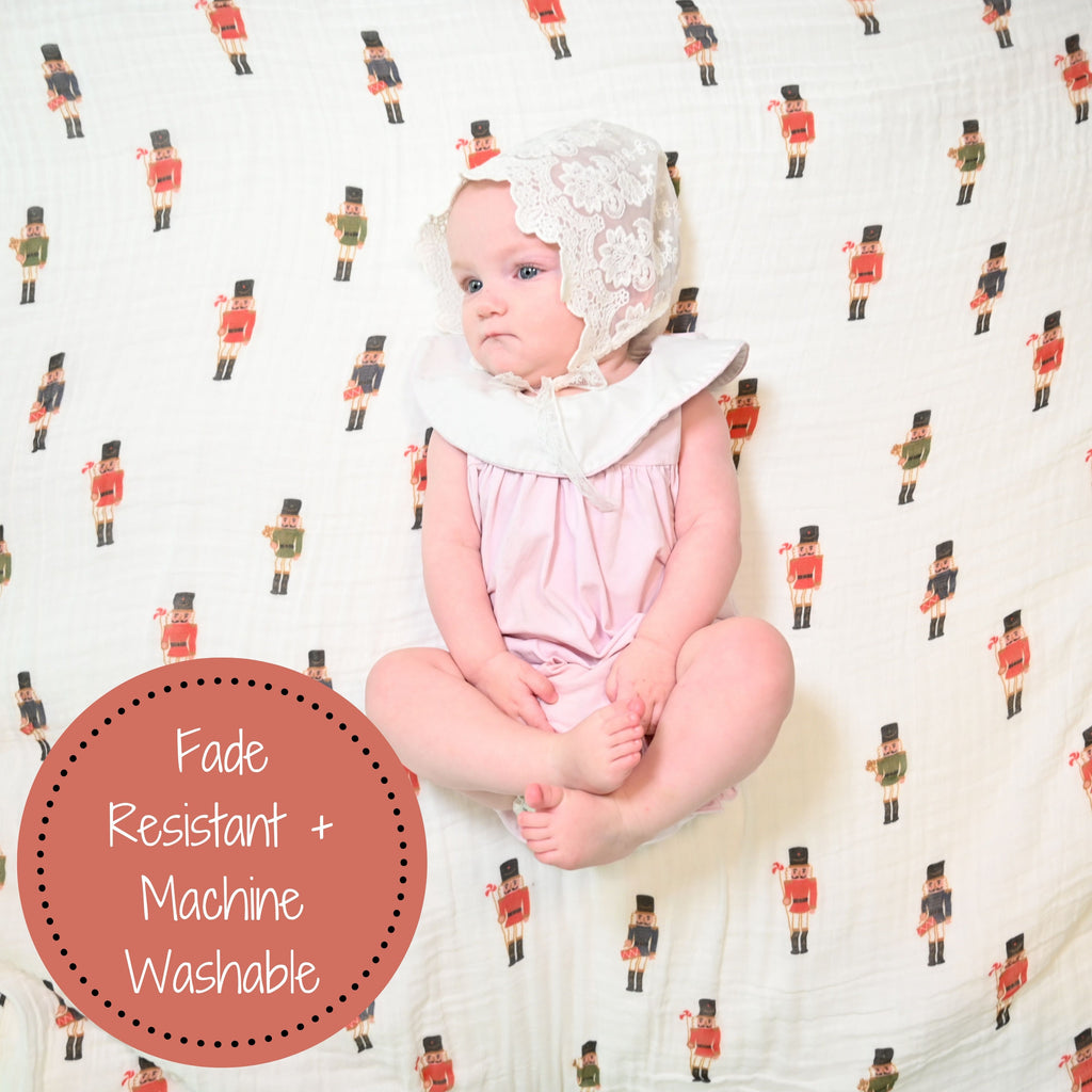 A happy baby girl with a radiant smile, against the enchanting backdrop of the Nutcracker Magic 100% Muslin Cotton Swaddle Blanket - 47" x 47", radiating joy and warmth