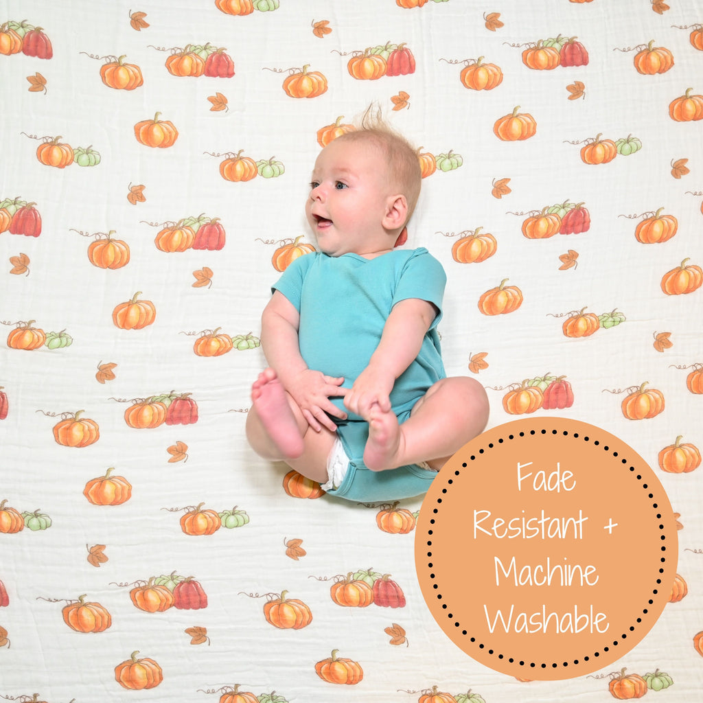 A cheerful baby boy with an infectious smile against the backdrop of a 100% Muslin Cotton Pumpkin Swaddle Blanket - 47" x 47", radiating warmth and happiness in the heart of the fall season.