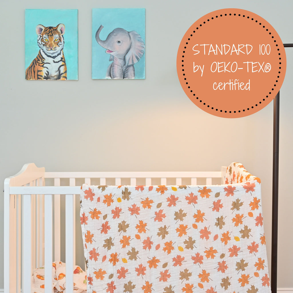 The Fall Leaves Muslin Swaddle Blanket - 47" x 47" beautifully draped on a crib, adding a touch of autumn charm to your baby's nursery.