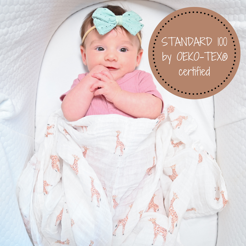 A happy baby girl with a heartwarming smile, snugly cocooned in the Giraffe Dreams Muslin Swaddle Blanket - 47" x 47", resting peacefully in her bassinet, surrounded by the whimsy of giraffes.