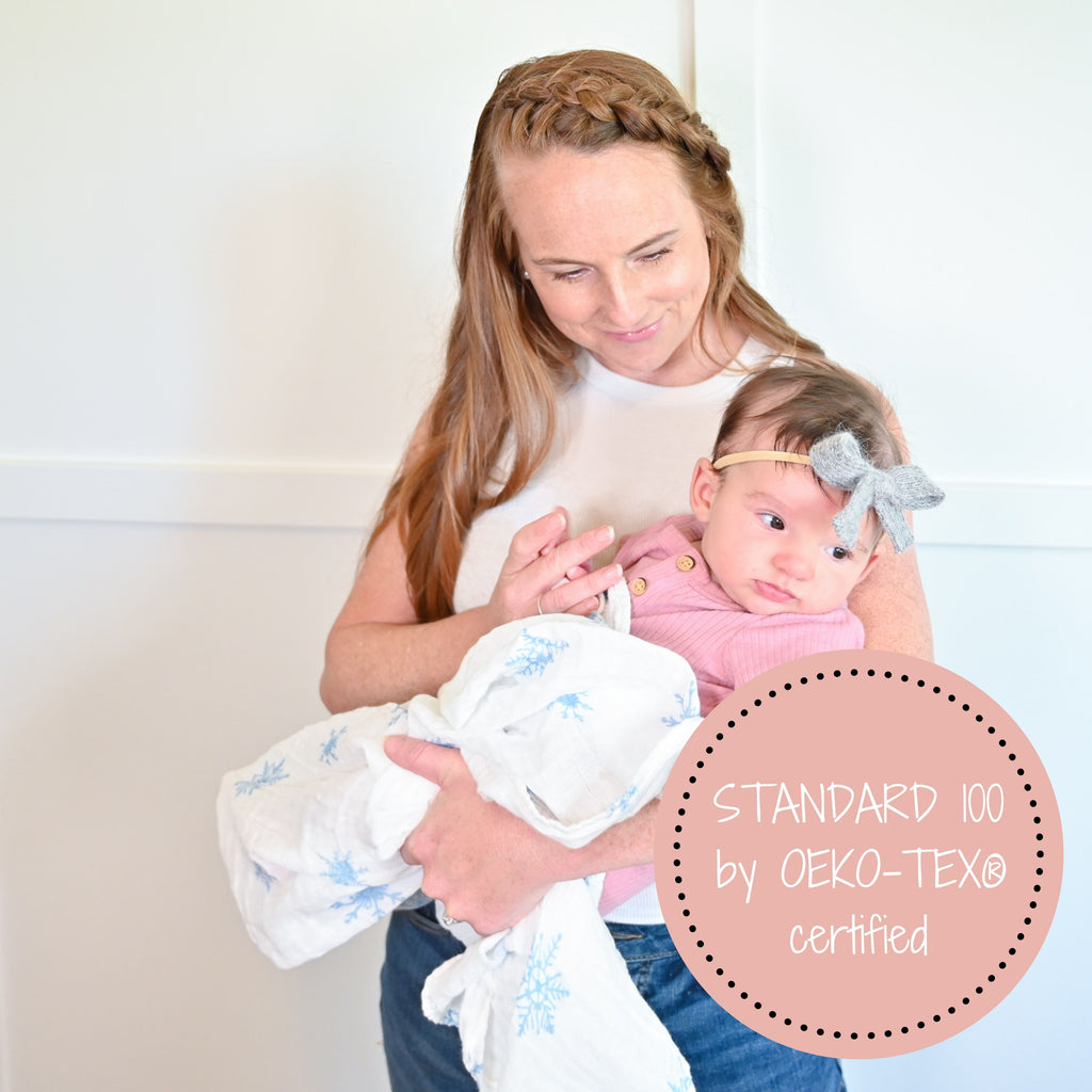 A loving mom cradling her baby in the Snowflake Elegance Muslin Swaddle Blanket - 47" x 47", enveloping them in warmth and wintery charm.