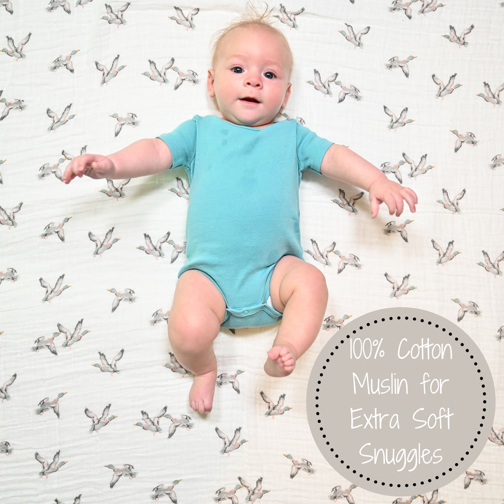 A joyful baby boy with a heartwarming smile, framed by the Mallard Magic 100% Muslin Cotton Swaddle Blanket - 47" x 47", radiating happiness and the whimsy of mallard ducks